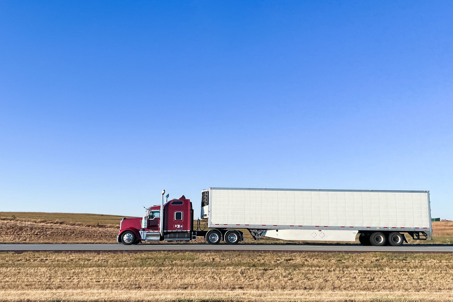 Right-Aligned Maroon & White Semi Truck on Interstate 70 Driving West across Kansas with Copy Space